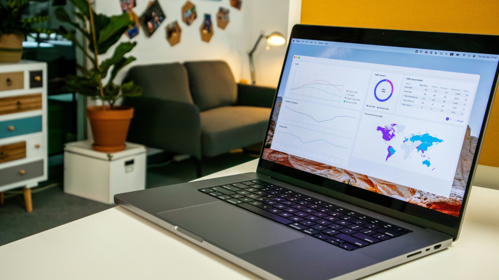 Offenes Laptop mit Daten Dashboard auf Schreibtisch in modernem Büro mit Sofa und Zimmerpflanzen